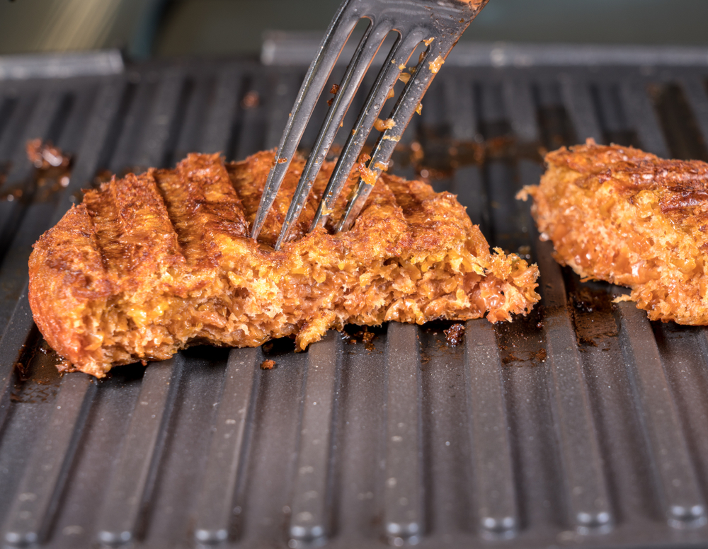 Detailní záběr na rostlinné masové kuličky pro vegetariánské hovězí hamburgery, které se grilují na rozpálené pánvi.